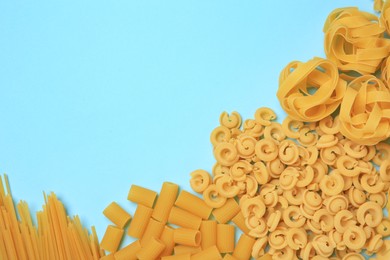 Different types of pasta on light blue background, flat lay. Space for text