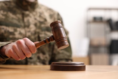 Law concept. Man in military uniform with gavel at wooden table, closeup. Space for text