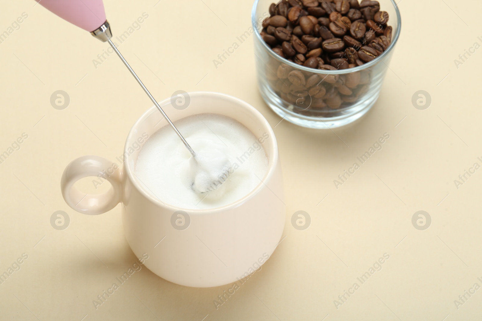 Photo of Whisking milk in cup with mini mixer (milk frother) on beige background