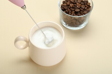 Whisking milk in cup with mini mixer (milk frother) on beige background