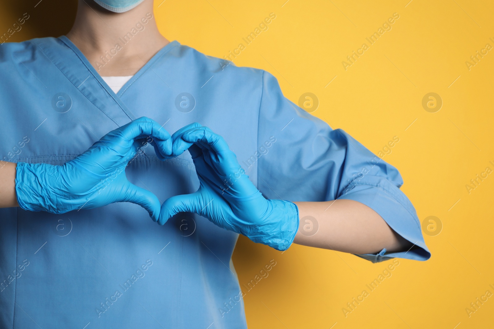 Photo of Doctor making heart with hands on yellow background, closeup