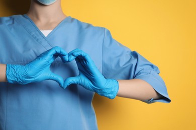 Doctor making heart with hands on yellow background, closeup