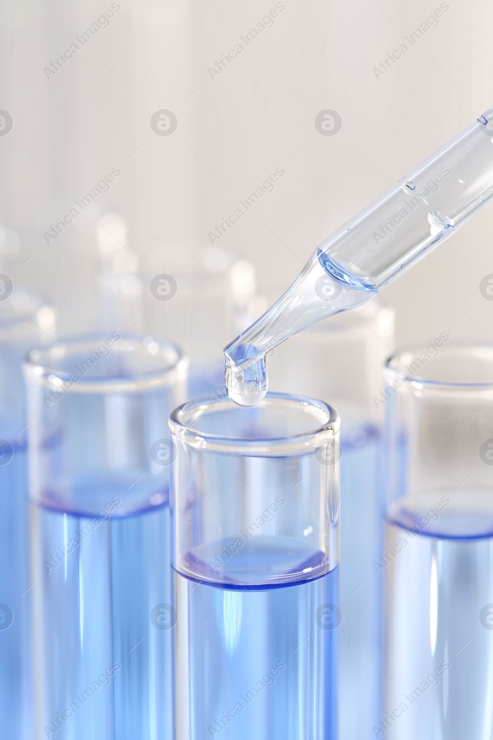 Photo of Laboratory analysis. Dripping light blue liquid from pipette into glass test tube on blurred background, closeup