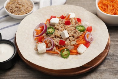 Photo of Delicious tortilla with tuna, vegetables and cheese on wooden table. Cooking shawarma