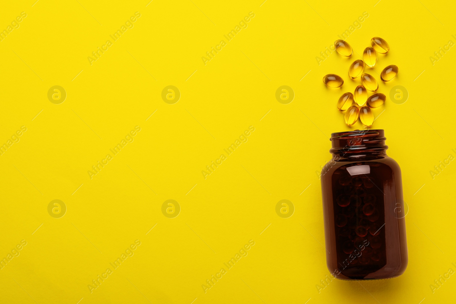 Photo of Overturned bottle with dietary supplement capsules on yellow background, flat lay. Space for text