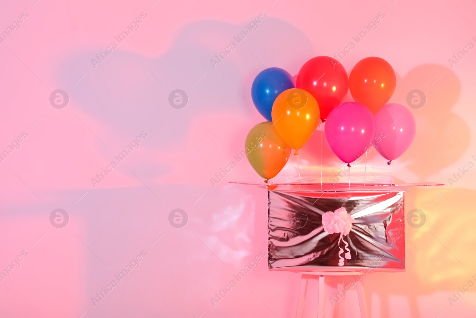 Photo of Gift box with bright air balloons on color background. Space for text