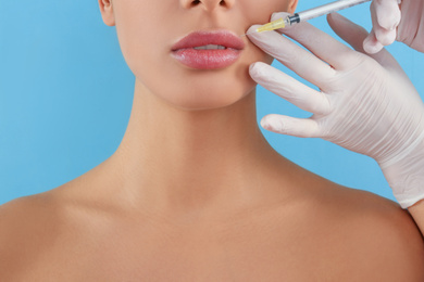 Photo of Woman getting lip injection on light blue background, closeup