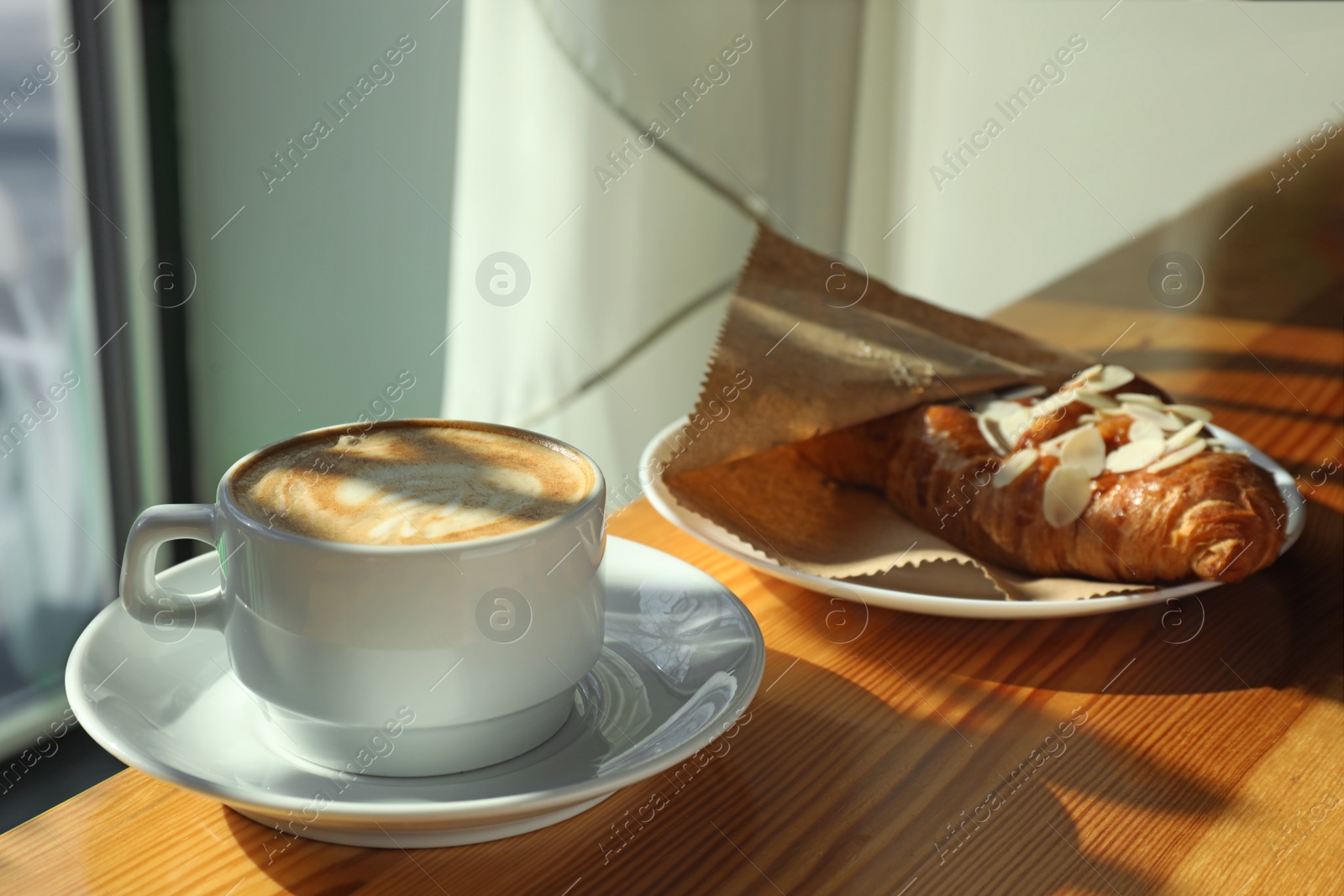 Photo of Cup of fresh aromatic coffee and croissant at table in cafe