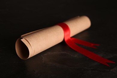 Rolled student's diploma with red ribbon on black table