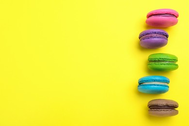 Photo of Delicious colorful macarons on yellow background, flat lay. Space for text