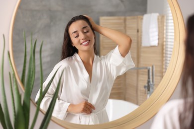 Photo of Beautiful young woman near mirror in bathroom. Hair care