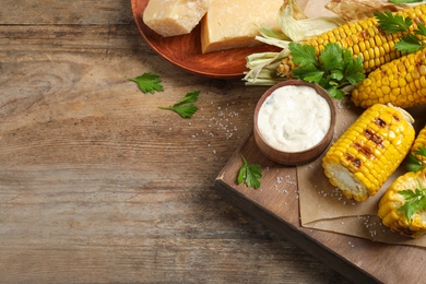 Photo of Delicious grilled corn cobs on wooden table, above view. Space for text