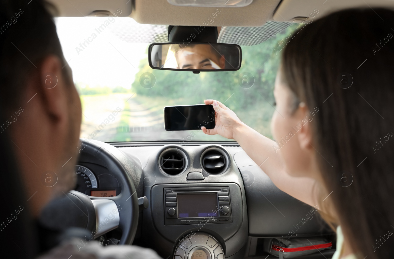 Photo of Young couple taking selfie in car on road trip. Back view