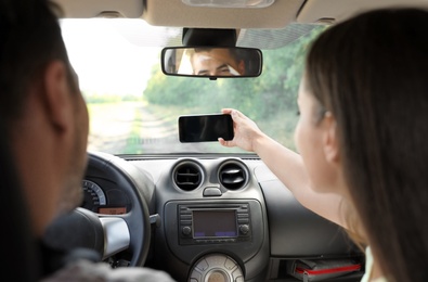 Photo of Young couple taking selfie in car on road trip. Back view