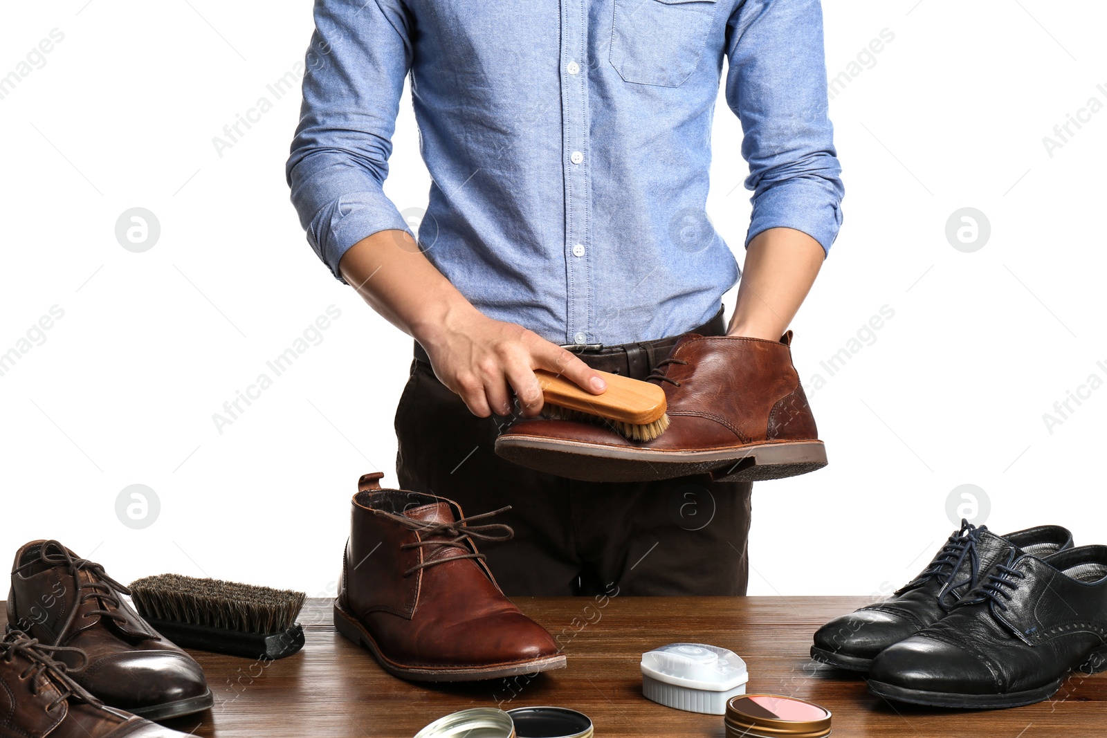 Photo of Man cleaning leather shoe at wooden table against white background, closeup