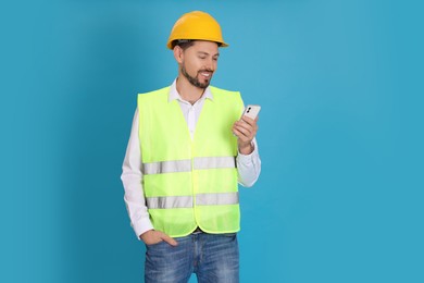 Male industrial engineer in uniform with phone on light blue background