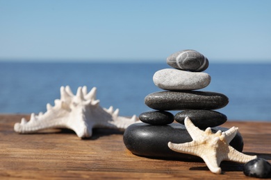 Photo of Stack of stones and starfishes on wooden pier near sea, space for text Zen concept