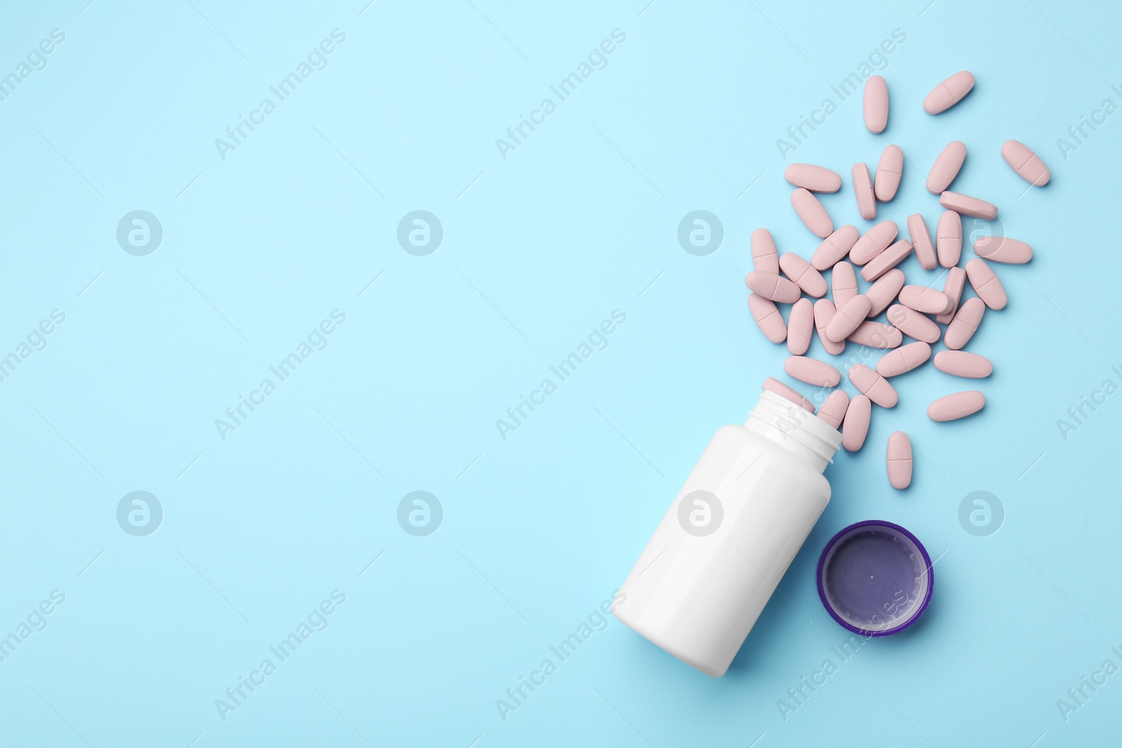 Photo of Vitamin pills, lid and bottle on light blue background, flat lay. Space for text