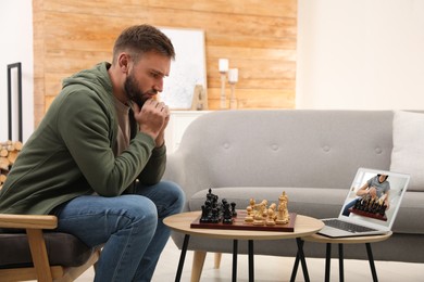 Image of Thoughtful young man playing chess with partner via online video chat in living room