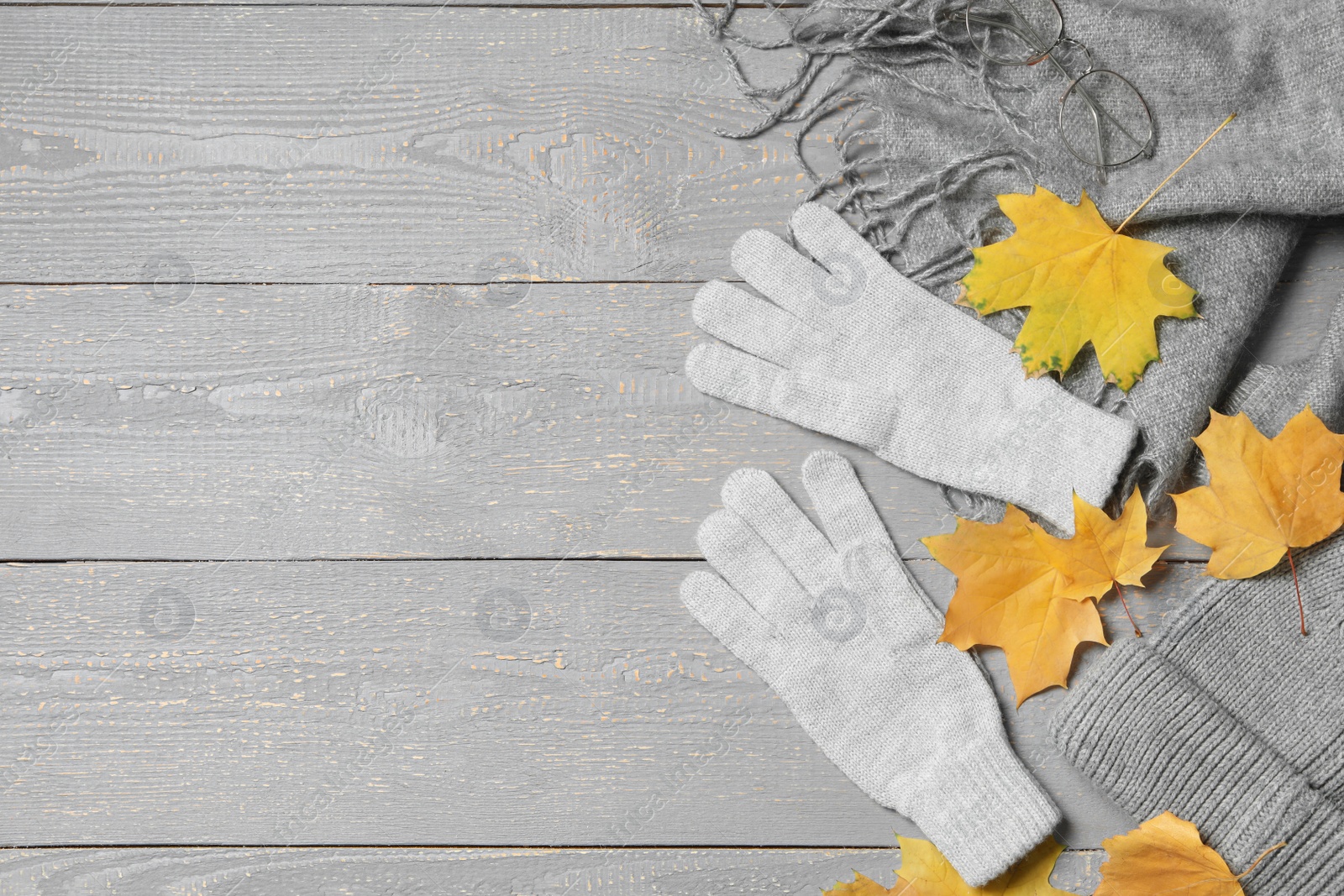 Photo of Flat lay composition with stylish woolen gloves and dry leaves on grey wooden table. Space for text