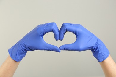 Photo of Person in medical gloves showing heart gesture on grey background, closeup of hands