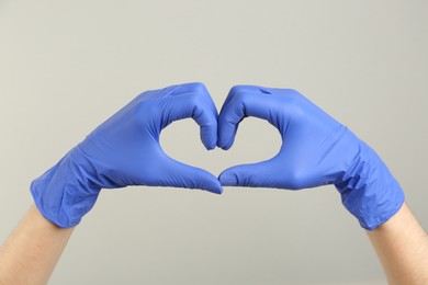 Person in medical gloves showing heart gesture on grey background, closeup of hands