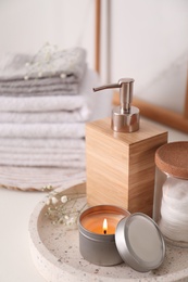 Photo of Tray with soap dispenser, cotton pads and burning candle on countertop in bathroom