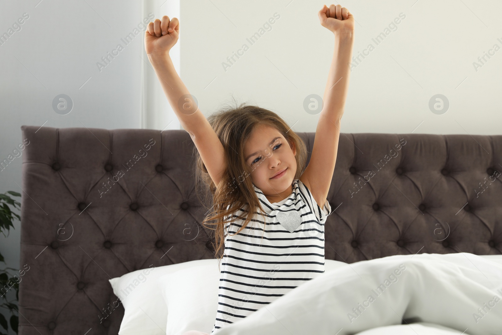 Photo of Cute little girl stretching after sleep in comfort bed