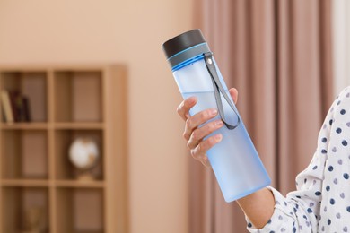 Photo of Woman with bottle of water in room, closeup. Space for text