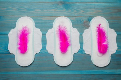 Photo of Menstrual pads with pink feathers on turquoise wooden background, flat lay