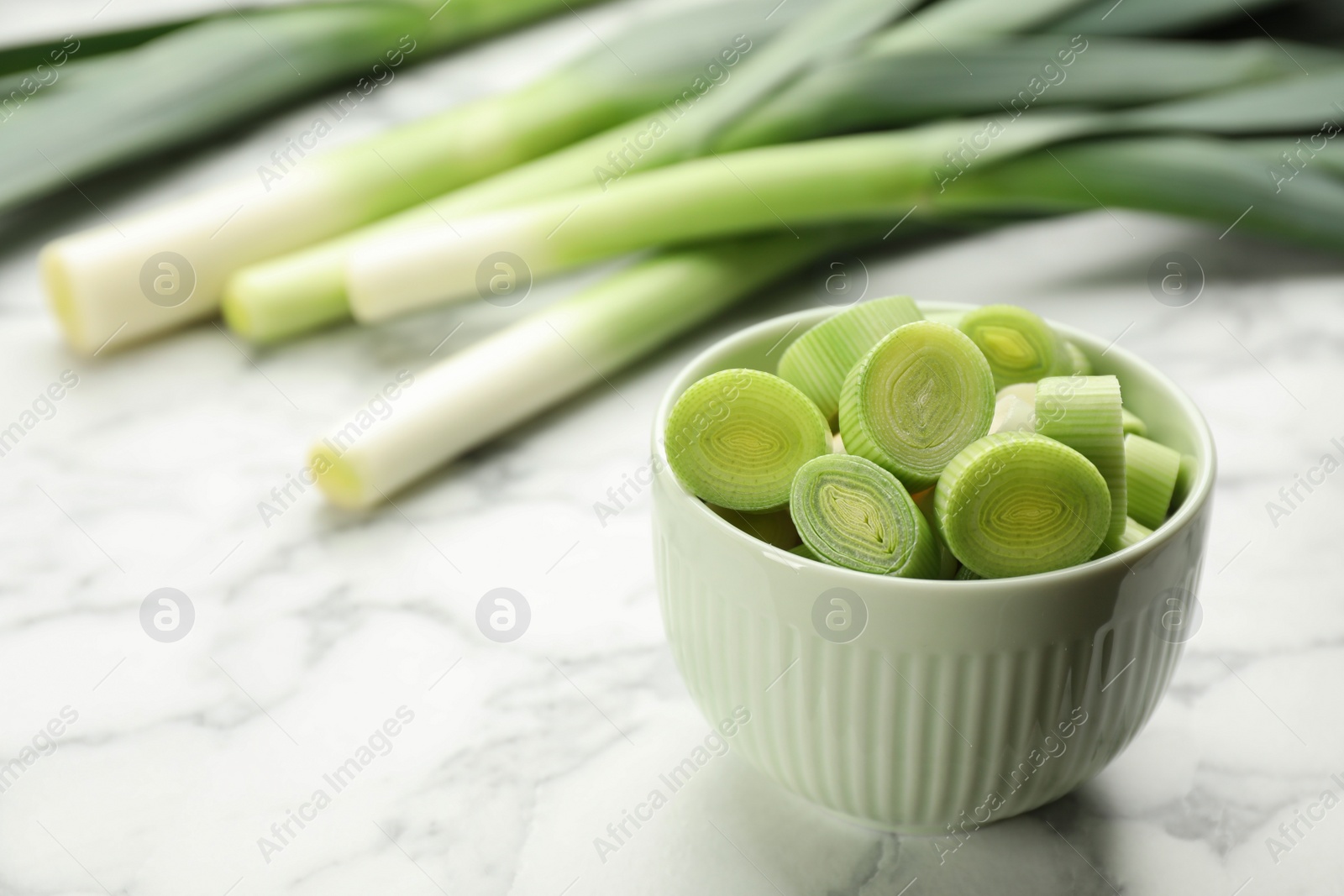 Photo of Cut fresh raw leek in bowl on white marble table, closeup. Space for text