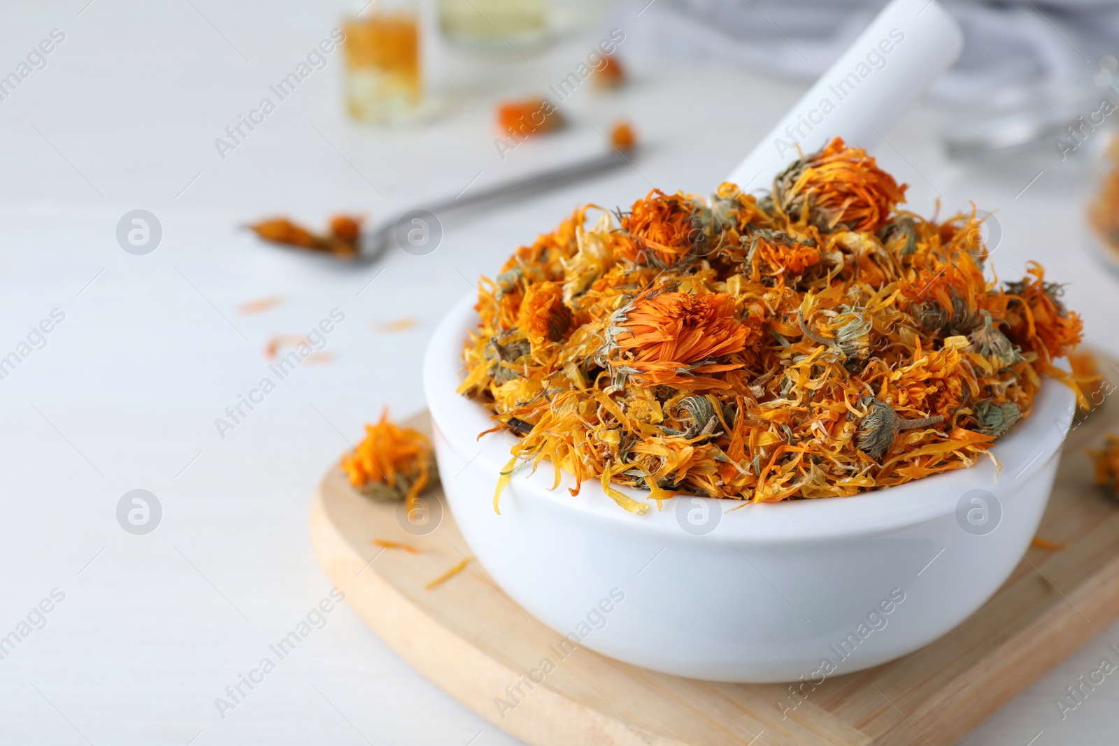 Photo of Mortar of dry calendula flowers on white table. Space for text