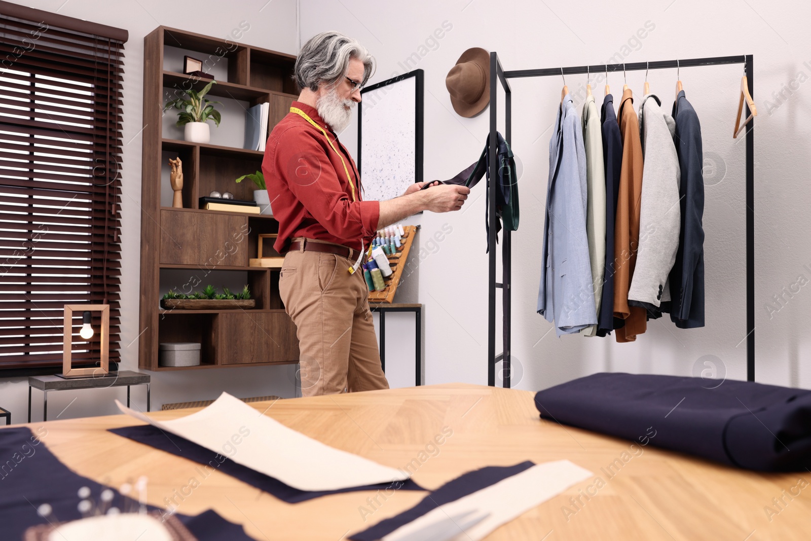 Photo of Professional tailor choosing tie near rack in workshop