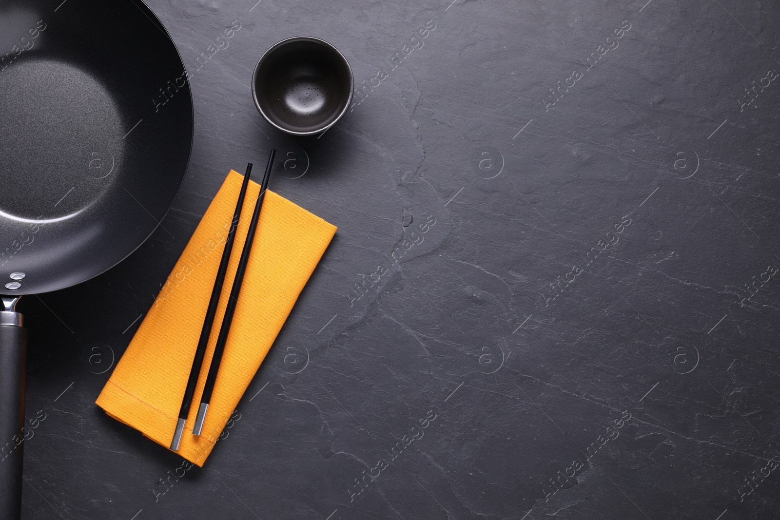 Photo of Empty iron wok, sauce bowl and chopsticks on black table, flat lay. Space for text