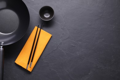 Empty iron wok, sauce bowl and chopsticks on black table, flat lay. Space for text