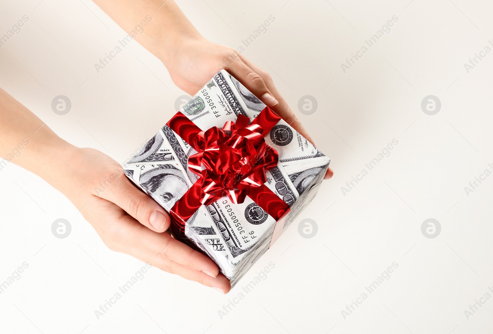 Photo of Woman holding gift box wrapped in decorative paper with dollar pattern on white background, closeup