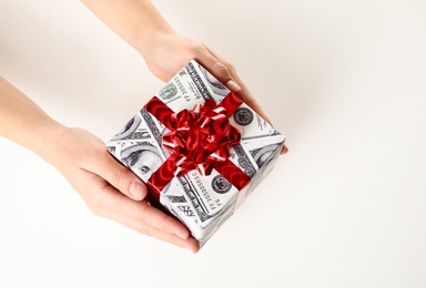 Woman holding gift box wrapped in decorative paper with dollar pattern on white background, closeup