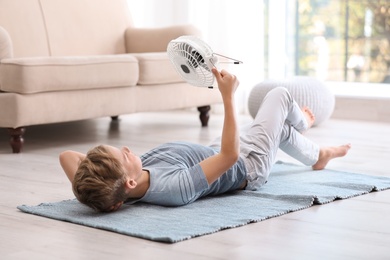 Photo of Little boy with fan relaxing at home. Summer heat