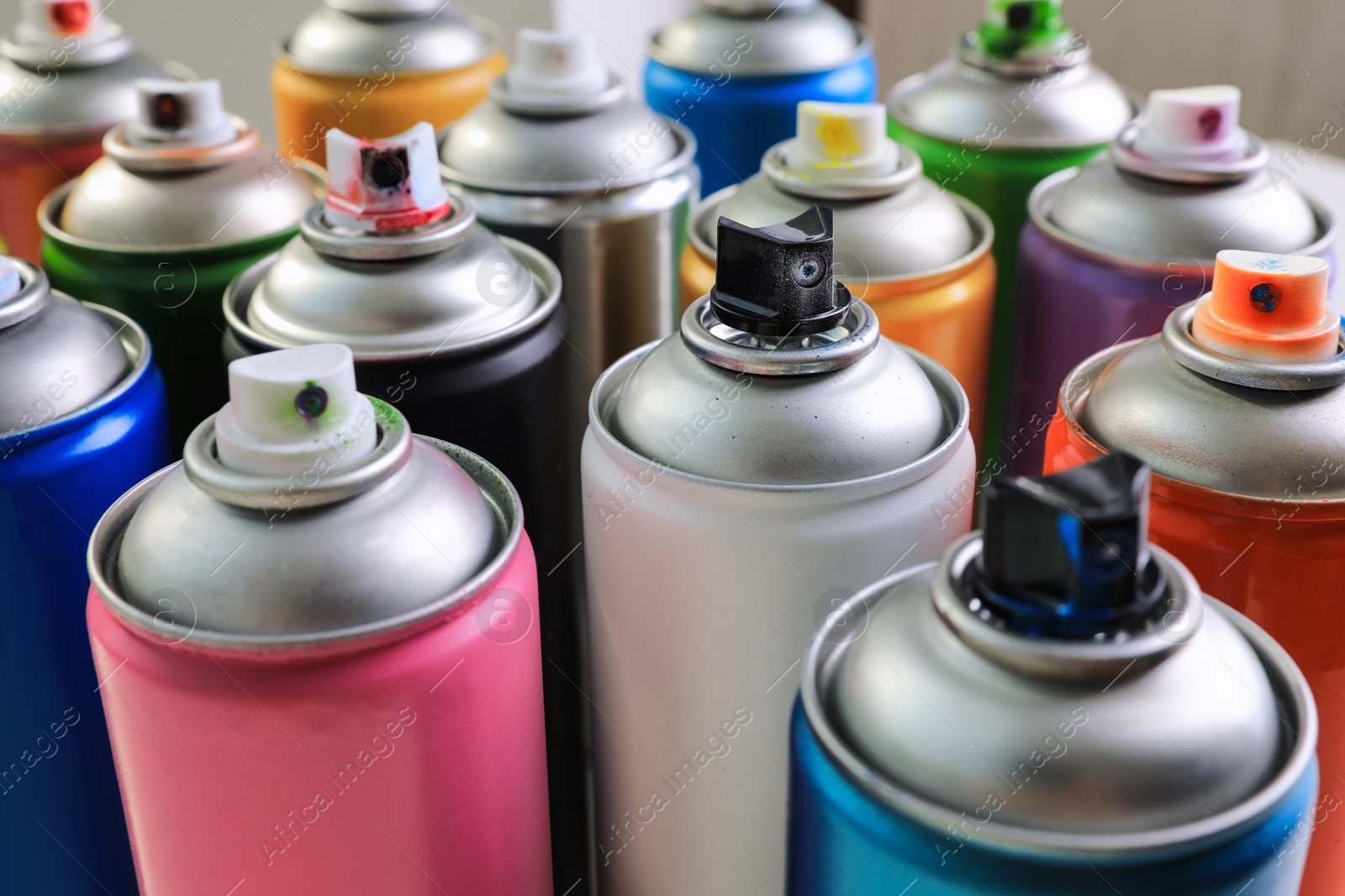 Photo of Cans of different graffiti spray paints on blurred background, closeup