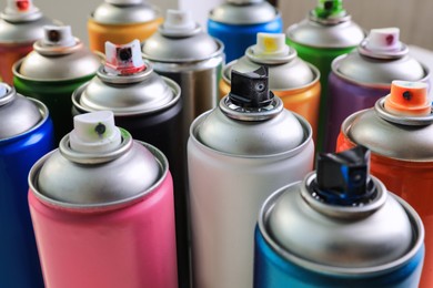 Cans of different graffiti spray paints on blurred background, closeup