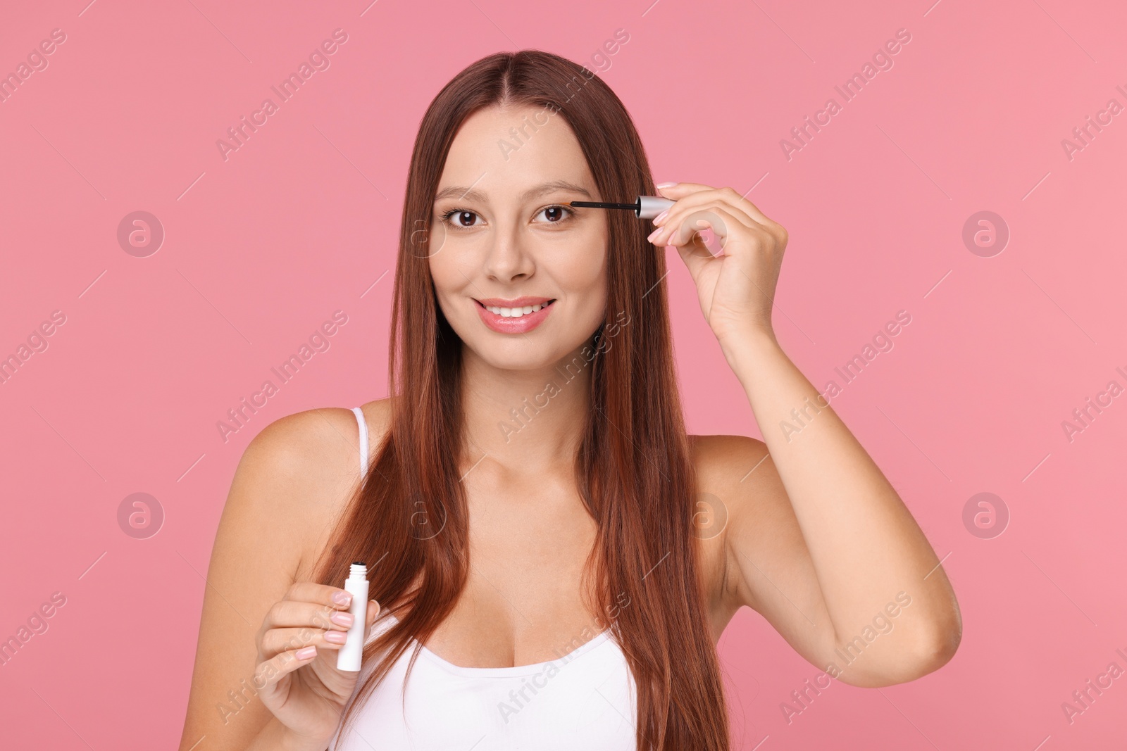 Photo of Beautiful woman applying serum onto eyelashes on pink background