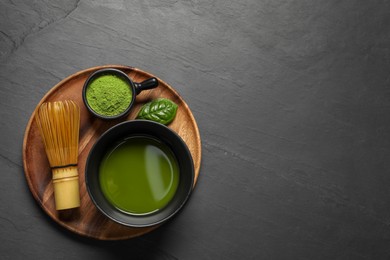 Photo of Cup of fresh matcha tea, bamboo whisk and green powder on black table, top view. Space for text