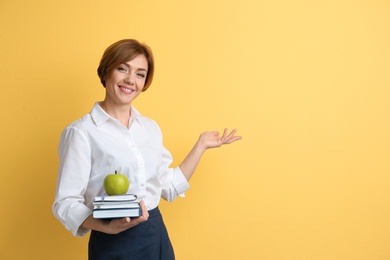 Photo of Portrait of female teacher with notebooks and apple on color background