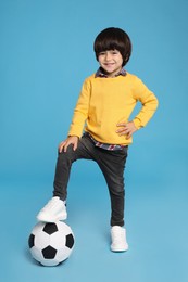 Cute little boy with soccer ball on light blue background