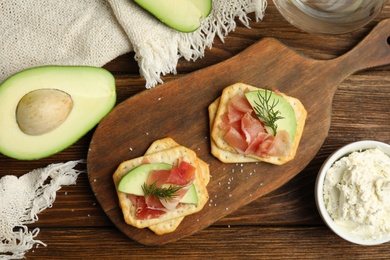 Photo of Delicious crackers with avocado, prosciutto and dill on wooden table, flat lay