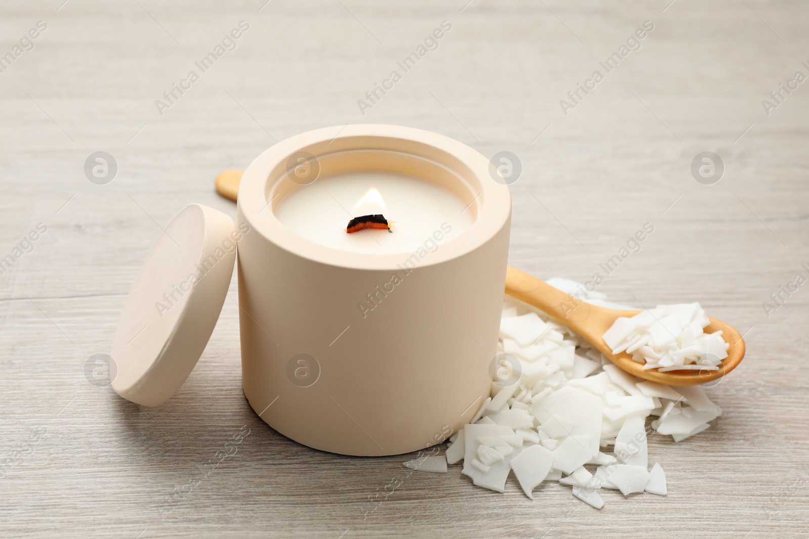 Photo of Burning soy candle, wax flakes and spoon on wooden table