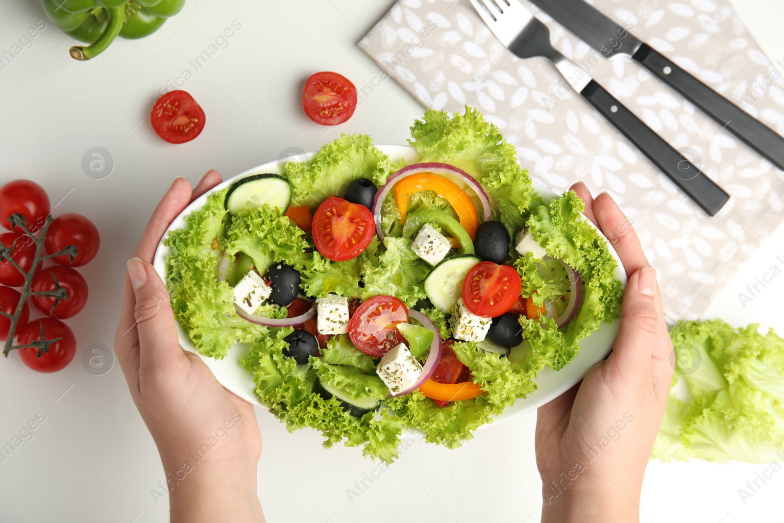 Photo of Woman holding plate of tasty fresh Greek salad over white table, top view