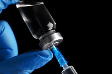 Photo of Doctor filling syringe with medication on black background, closeup. Vaccination and immunization