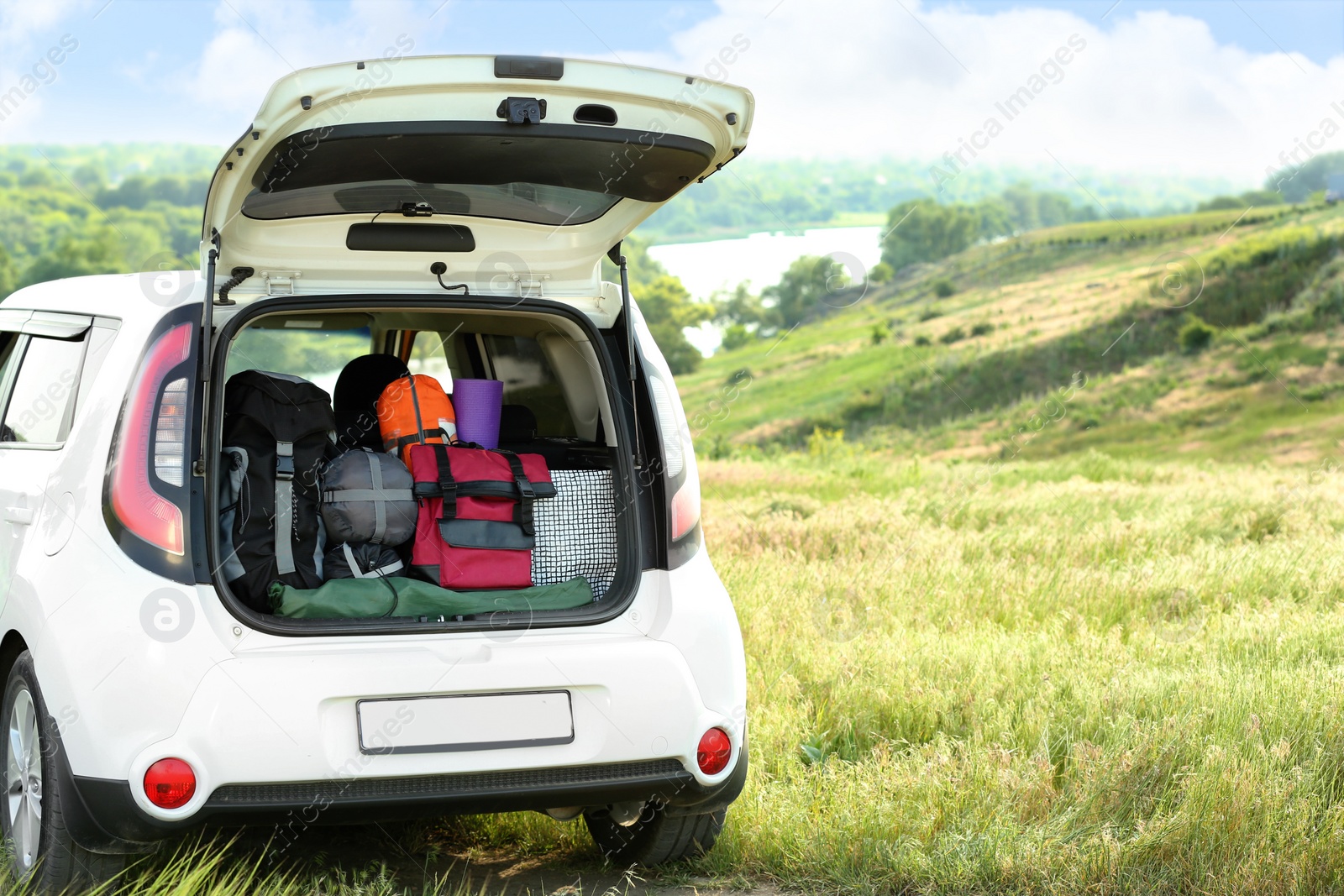 Photo of Car with camping equipment in trunk on green field. Space for text