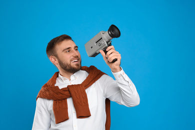 Young man with vintage video camera on light blue background